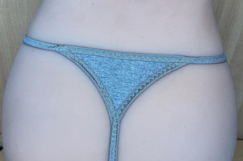 May include: A light gray thong with a delicate lace trim. The thong is made of a soft, stretchy fabric.