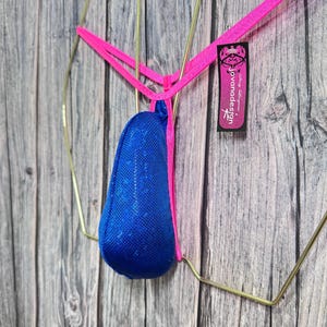 May include: A blue sequined thong with a pink waistband and gold-colored metal accents. The thong features a small tag with the text "jovanadesign". The garment is displayed against a wooden background.
