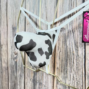 May include: White mesh underwear with a black and white cow print design. The underwear has a thin white strap with a small tag that says "Jovahadesign".
