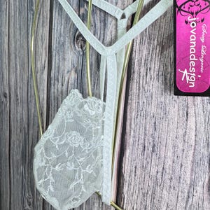 K&ouml;nnte beinhalten: Hellgr&uuml;ner String-Tanga mit floraler Spitze vorne. Der String h&auml;ngt an einem goldfarbenen Kleiderb&uuml;gel. Ein pinkfarbenes Etikett mit dem Text "Jovanadesign" ist sichtbar.