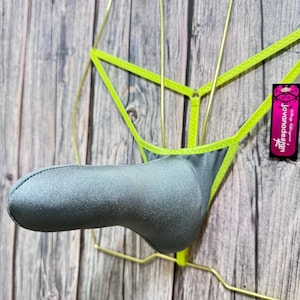 Puede incluir: Una tanga gris con ribete verde neón, exhibida en una percha de alambre dorado. La prenda interior tiene una bolsa acolchada y una pequeña etiqueta con el texto "Jovanadesign". El fondo es una superficie de madera.