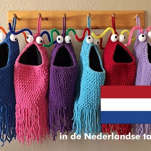 May include: Six crocheted hanging toy pouches with colourful fringe and googly eyes. The pouches are in blue, pink, purple, red, and lavender. The pouches are hanging from a wooden rack. The Dutch flag is in the bottom right corner of the image. The text "in de Nederlandse taal" is at the bottom of the image.