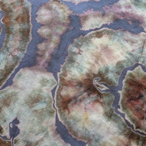 May include: A fabric featuring a tie-dye pattern with organic, swirling shapes in shades of muted blue, earthy brown, soft green, and cream. The design consists of rounded, cloud-like forms separated by distinct, dark blue-grey lines.