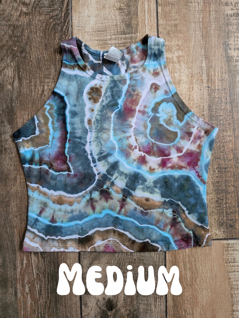 Pode incluir: Um top curto sem mangas com um padr&atilde;o tie-dye de faixas rodopiantes em azul, castanho, branco e magenta. A pe&ccedil;a tem um decote alto e uma etiqueta interior branca na gola. A palavra MEDIUM est&aacute; impressa a branco na parte inferior.