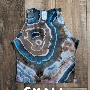 Pode incluir: Um top curto sem mangas com um padr&atilde;o tie-dye inspirado em geodos em tons de castanho, azul e branco. A pe&ccedil;a tem um decote alto e uma etiqueta interior branca na gola. A palavra SMALL est&aacute; impressa a branco na parte inferior.
