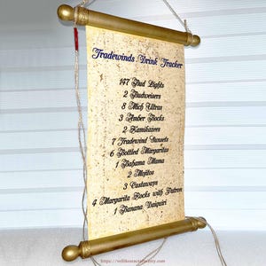 Könnte beinhalten: Eine Getränke-Tracker-Rolle mit dem Text "Tradewinds Drink Tracker" in blauer Schrift. Die Rolle listet verschiedene Getränke und Mengen auf, darunter Bud Lights und Margaritas. Die Rolle ist goldfarben mit tanfarbenem Papier.