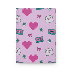 May include: A hardcover journal with a repeating pattern of pixelated pink hearts, cassette tapes, bows, envelopes with hearts, and square polaroid-style photos on a light purple background. The journal is closed and has a clean, minimalist design.