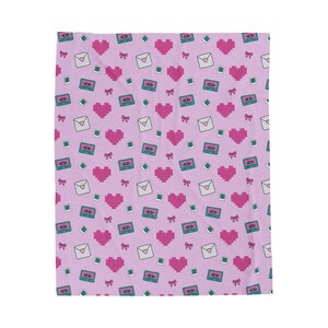 May include: A light pink blanket with a repeating pattern of pixelated pink hearts, cassette tapes, envelopes, bows, and diamonds. The blanket is made of a soft material and is suitable for a bed or couch.
