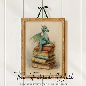 May include: A framed print featuring a teal dragon perched atop a stack of books. The dragon has green wings and is set against a soft, neutral background. The frame is gold, and the print is suspended by a green ribbon. The text "The Fabled Wall" is at the bottom.