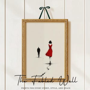 May include: A framed art print with a minimalist illustration of two figures, one in a red dress, on a white background. The gold frame is suspended by a green ribbon. The text at the bottom reads "The Fabled Wall".