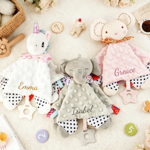 Puede incluir: Tres mantitas de apego de peluche con forma de unicornio blanco, elefante gris y rat&oacute;n rosa. Cada manta tiene una textura de puntos, una parte inferior con lunares blancos y negros, un mordedor en forma de estrella y los nombres bordados Emma, Isabel y Greace.