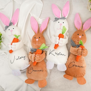 May include: Four plush bunny rabbits with carrot accents. The bunnies are white and brown with black and white checkered ribbon accents. The bunnies are personalized with the names "Victory", "Kristen", "Grace", and "Samuel".