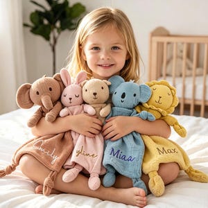 May include: A young girl holds five plush animal security blankets: an elephant, a bunny, a bear, a koala, and a lion. Each animal is a different color, with a matching blanket. The blankets are personalized with names.