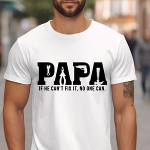 Könnte beinhalten: Weißes T-Shirt mit einer schwarzen Grafik, auf der "PAPA" mit in die Buchstaben integrierten Werkzeugen steht. Der Text unter der Grafik lautet "Wenn er es nicht reparieren kann, kann es niemand."