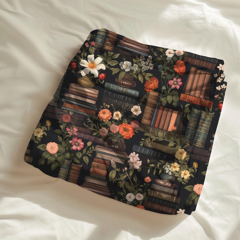 Peut inclure: Tissu sombre avec un motif de livres et de fleurs. Le motif pr&eacute;sente des piles de livres, des vases et des fleurs aux teintes orange, rose et blanc. Le tissu est pos&eacute; sur un fond blanc.