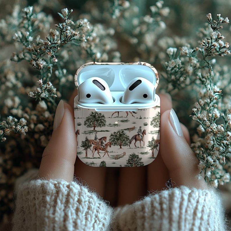 May include: White wireless earbuds in a case with a beige equestrian scene design. The case is open, revealing the earbuds. The background is blurred with white flowers.