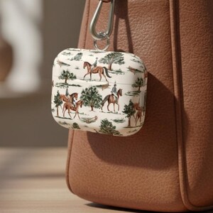 May include: A white AirPod case with a repeating pattern of brown horses and riders, trees, and foliage. The case is attached to a brown leather bag. Text at the bottom reads: BEST HORSE LOVER TECH GIFT.