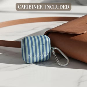 May include: A protective case for wireless earbuds featuring vertical stripes in shades of dark blue and light blue. The name Michelle is printed in white script on the front. A silver metal carabiner is attached to the side. Text reads CARIBINER INCLUDED.