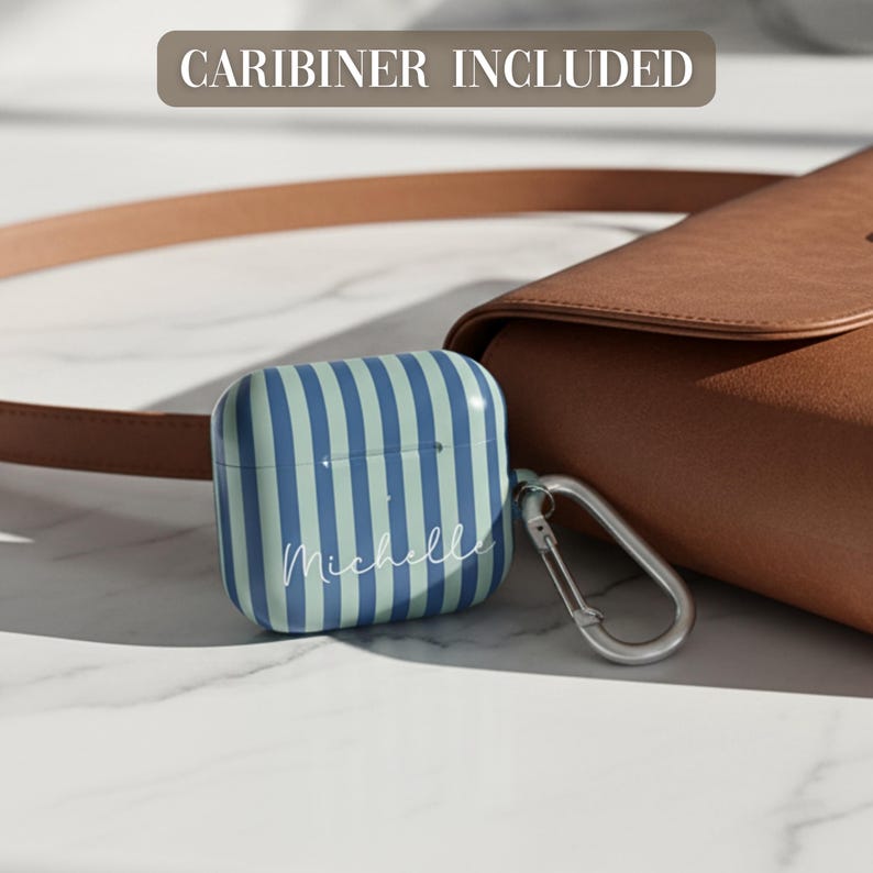 May include: A protective case for wireless earbuds featuring vertical stripes in shades of dark blue and light blue. The name Michelle is printed in white script on the front. A silver metal carabiner is attached to the side. Text reads CARIBINER INCLUDED.