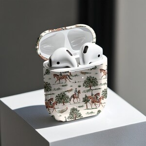 May include: White wireless earbuds inside a case with a cream-colored equestrian scene design. The case is open, revealing the earbuds. The design features riders on horseback, trees, and a fence.