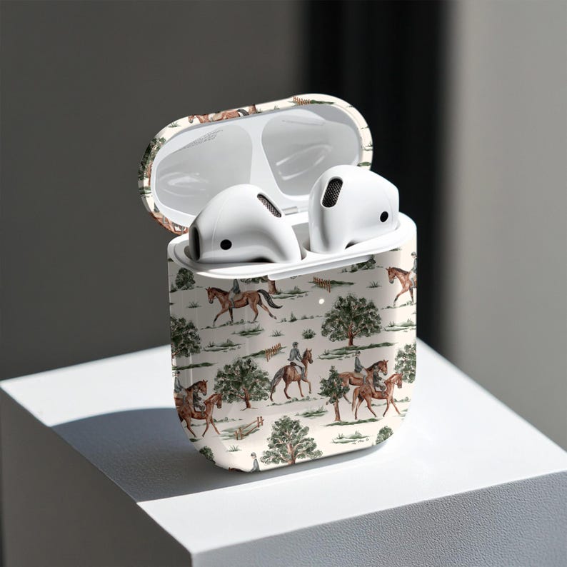 May include: White wireless earbuds inside a case with a cream-colored equestrian scene design. The case is open, revealing the earbuds. The design features riders on horseback, trees, and a fence.