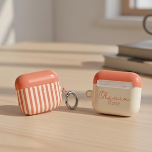 May include: Two peach and white AirPod cases. One case has vertical stripes, the other has the name "Olivia Rose" in cursive. Both cases have a peach-colored top and a silver carabiner clip.