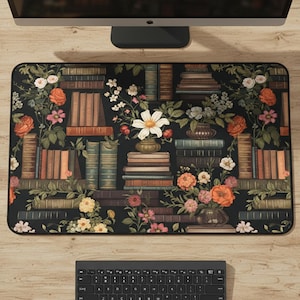 Könnte beinhalten: Rechteckige schwarze Schreibtischunterlage mit Blumen- und Bücherregal-Design. Die Unterlage zeigt Stapel von Büchern in verschiedenen Farben, durchsetzt mit orangefarbenen, rosa und weißen Blumen. Ein Computermonitor und eine Tastatur sind sichtbar.