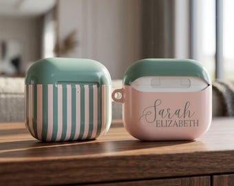 May include: Two protective cases for wireless earbuds. One case features vertical sage green and light pink stripes. The other case is solid light pink with a sage green lid and the name Sarah Elizabeth printed in a dark green cursive script font.