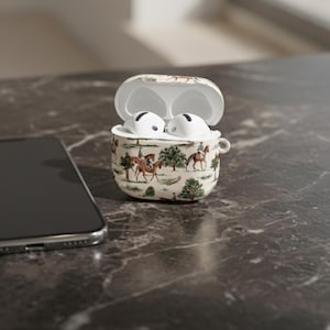May include: An open, cream-colored AirPods case with a horse-themed design, containing white earbuds. The case features a repeating pattern of riders on horseback, trees, and foliage. A smartphone is visible in the background.