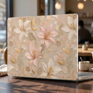 Könnte beinhalten: Eine Laptop-Hülle mit einem strukturierten, malerischen Blumenmuster aus zartrosa und cremefarbenen Lilien, feinen goldfarbenen Blättern und kleinen hellrosa Blütenclustern auf einem neutralen, warmen beigen Hintergrund.