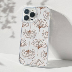 May include: A clear phone case with a white background and a pattern of brown ginkgo leaves.