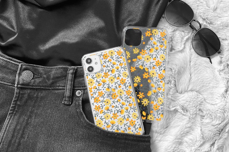 Clear phone case with small yellow flower print. There are 2 cases, one on a white iPhone case and the other is loose. They're both in a black jeans pocket, to enhance a total black outfit: pants, top and glasses.