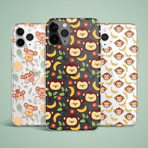 May include: Three phone cases featuring monkey and banana designs. One case has a black background with red flowers, bananas, and monkey faces. The other two cases have white backgrounds with monkeys and bananas. The cases are made of clear plastic.