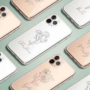 Puede incluir: Una colección de fundas para iPhone doradas y blancas con diseños florales y nombres personalizados. Los nombres en las fundas son Sylvie, Charlie, Molly y Bertie.