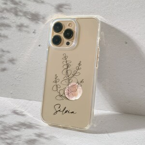 May include: A clear phone case with a gold background and a black line drawing of a plant with a pink shell. The name "Silvia" is written in black cursive at the bottom of the case.