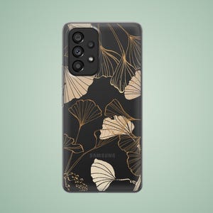 May include: A clear phone case with a black background and a gold leaf pattern. The case has a cutout for the camera lens and the Samsung logo is visible on the back.