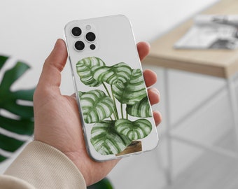 May include: A clear phone case with a white background and a green and white tropical plant design. The case is designed for a smartphone with a triple camera lens.
