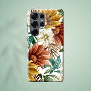 Op de afbeelding: Een smartphonehoesje met een bloemenpatroon. De hoes toont grote bloemen in gele, oranje en bruine tinten, tegen een witte achtergrond. Groene bladeren en kleinere witte bloemen maken het ontwerp compleet. De hoes heeft een cameramodule.
