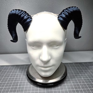 May include: A pair of dark blue, curved horns attached to a white head form. The horns have a textured, ridged appearance and are positioned on either side of the head. The head is on a silver scale.