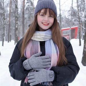 May include: A person wearing a gray knit hat, scarf, and gloves in a snowy forest. The gloves have an embroidered design. The scarf has a pastel color scheme of pink, blue, and white.