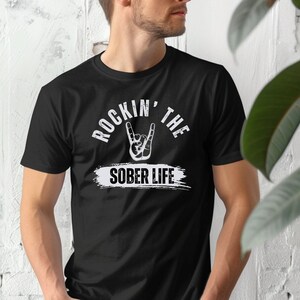 May include: Black t-shirt with a white graphic that says "Rockin' the Sober Life" with a rock and roll hand gesture.