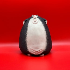 May include: A ceramic figurine of a black and white cat with a round, plump body. The cat has a white face and a black nose.