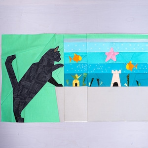 May include: A patchwork quilt block depicting a black cat and an underwater scene. The cat is set against a green backdrop, with the underwater scene including fish, a starfish, and a castle. The block is made from various fabric pieces.