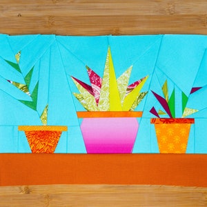 May include: Three potted plants with different colored pots and patterned fabric leaves. The plants are on a brown surface.