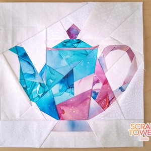 May include: A patchwork quilt block featuring a teal and pink teapot with a white background. The block is made up of many small pieces of fabric sewn together. The teapot is in the center of the block and is surrounded by a white border. The block is labeled "Scrap Tower Studio" in the bottom right corner.