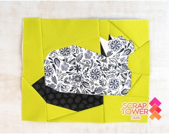 May include: A quilt block featuring a black and white floral print fabric in the shape of a bunny, surrounded by lime green fabric.