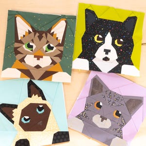 May include: Four fabric squares with geometric cat portraits. The cats have different patterns and colours, including brown tabby, black and white tuxedo, Siamese, and grey tabby designs. Each cat is set against a different background colour.