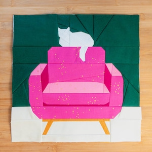 Może przedstawiać: Pikowany blok materiału przedstawiający różowy fotel ze złotymi nogami, białego kota i zielone tło. Fotel ma jasnoróżowe siedzisko i jest ozdobiony złotymi plamkami. Kot jest biały i siedzi na oparciu krzesła.