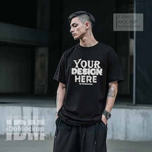 Könnte beinhalten: Ein schwarzes T-Shirt mit dem Text "YOUR DESIGN HERE" in Weiß mit einem Used-Look. Der Text wird von "By iDoMockup" in kleinerer weißer Schrift gefolgt.