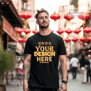May include: A black t-shirt with the text "招财进宝 YOUR DESIGN HERE By IDoMockup" in yellow. The shirt is being worn by a person standing in front of a red lantern backdrop.